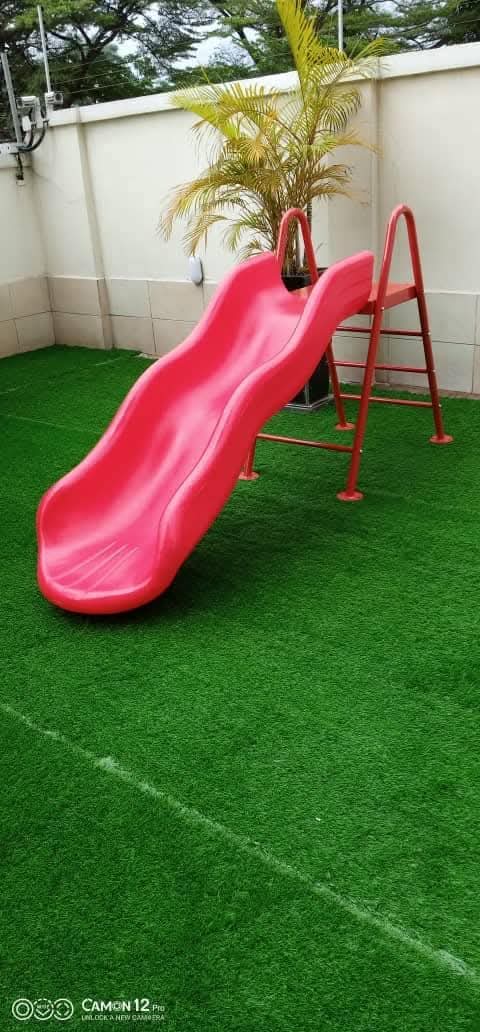 Red wave slide installed on garden artificial grass by Ere Ayo Mothercare Toys.