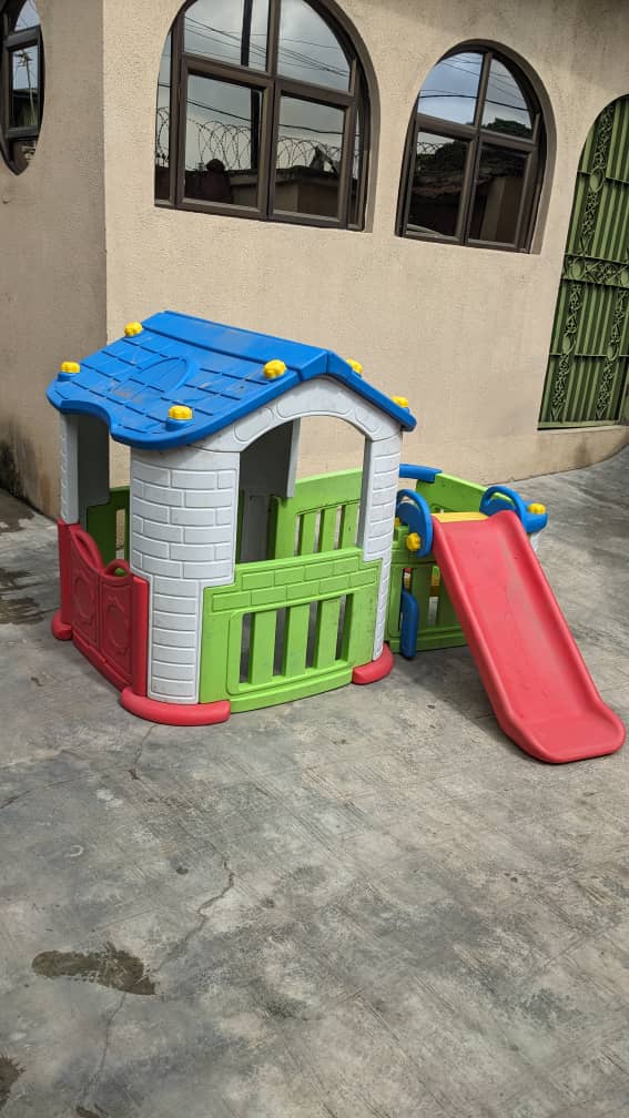 Plastic playhouse with an attached slide installed in a building courtyard by Ere Ayo Mothercare Toys.