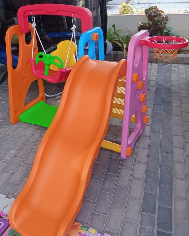 Outdoor toddler swing, slide and basketball combo set installed on a paved play area.
